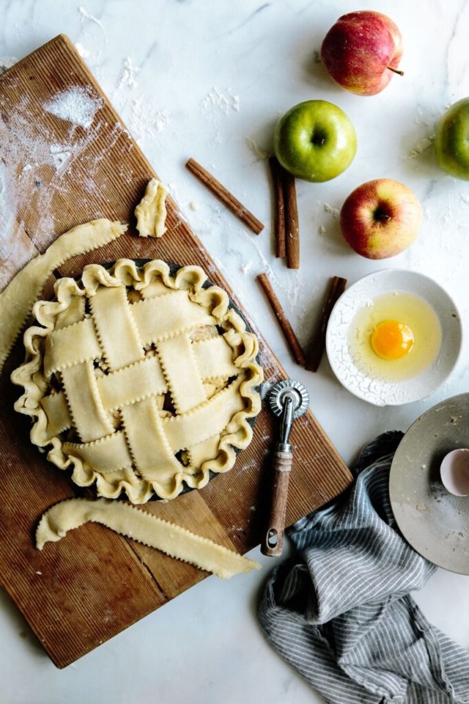 A freshly made Piehole apple pie ready to be baked, with cinnamon and apples near by.